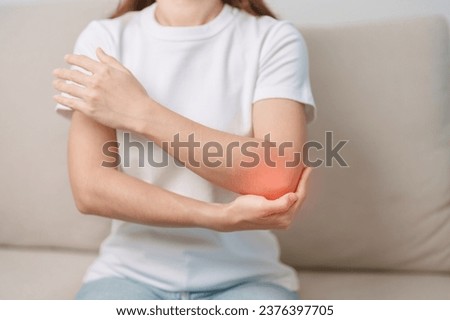 Woman having elbow ache during sitting on couch at home, muscle pain due to lateral epicondylitis or tennis elbow. injury, Health and medical concept Royalty-Free Stock Photo #2376397705