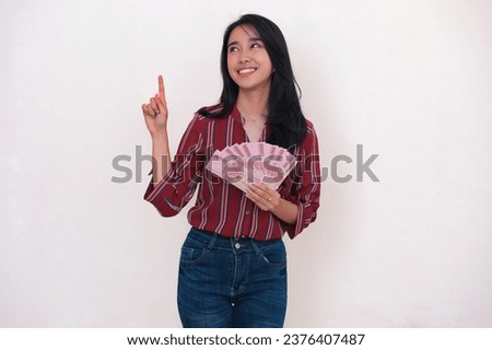 Excited expression of an Asian woman standing and holding some rupiah money for shopping Royalty-Free Stock Photo #2376407487