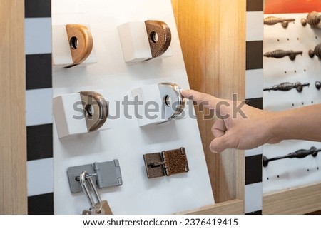 Designer hand pointing at fixed metal latch padlock staple on door hardware catalog in home design store. Stainless steel padlock hasp and staple collection. Door fitting part for safety and security Royalty-Free Stock Photo #2376419415