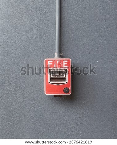 Fire alarm switch mounted on a wall painted gray.