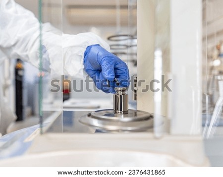 A operator's hand is holding steel calibration weight to place on the analytical balance. Concept of quality control in a laboratory. Royalty-Free Stock Photo #2376431865