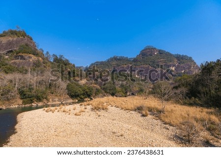 Scenic picture of the river, tall strange shaped rocks and burned orange grass in Wuyishan Scenic area, Fujian, China