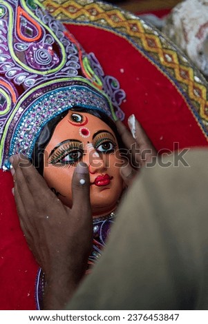 Hands of an unknown artist decorating face of Goddess Durga with use of selective focus on a particular part of the face, with rest of the face, the hands and everything else blurred. 