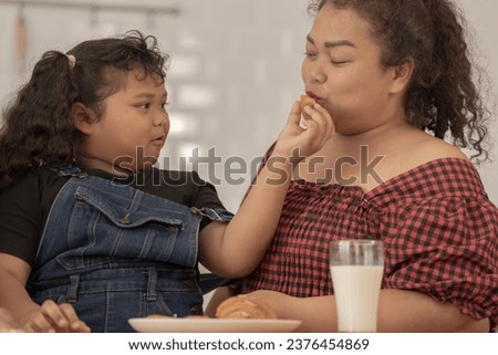 close up face of a Cute Asian girl eating a snack with family. Pretty Black Child Eating Snack At Home. Preschool Kid Having A Bite With Fresh Baked Biscuits.