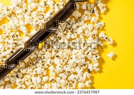 Scattered delicious popcorn and film stock on yellow background.