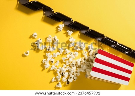 Classic striped bucket with delicious popcorn and film stock on yellow background.