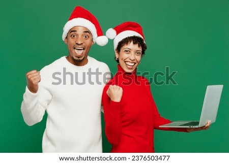 Merry fun winner young couple friends IT man woman wear red casual clothes Santa hat posing work hold use laptop pc computer isolated on plain green background. Happy New Year 2024 Christmas concept
