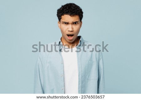 Young shocked irritated sad man of African American ethnicity wear shirt white t-shirt casual clothes look camera with opened mouth isolated on plain pastel light blue cyan background studio portrait Royalty-Free Stock Photo #2376503657