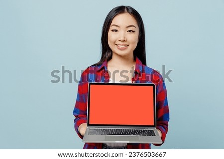 Young happy smiling fun woman of Asian ethnicity 20s wearing checkered shirt hold use work on laptop pc computer with blank screen workspace area isolated on plain pastel light blue color background. Royalty-Free Stock Photo #2376503667