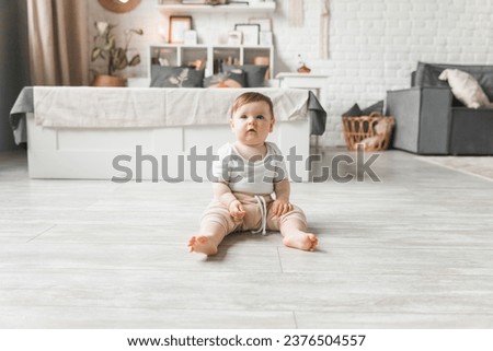 Portrait of a 7-9 month old baby in a home interior. A curious, smiling child explores the world around him. A cute baby is sitting on the floor. Royalty-Free Stock Photo #2376504557