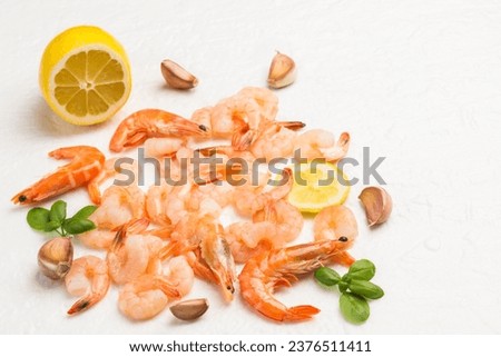 Shrimp, tiger prawns scattered on white background. Leaves of green basil, lemon, garlic and peppercorn. Delicious appetizing food. Top view
