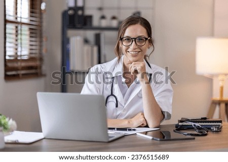 Young lady doctor in white medical uniform using laptop talking video conference call with senior doctor at desk,Doctor sitting at desk and writing a prescription for her patient Royalty-Free Stock Photo #2376515689