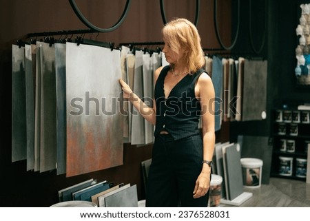 The sales girl demonstrates samples of decorative coatings in the interior of finishing materials. Palettes of dark and gray tones are presented.