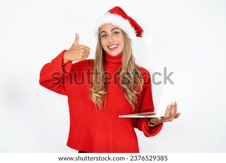 Beautiful attractive Beautiful hispanic woman wearing christmas hat hold netbook hand finger show thumb up
