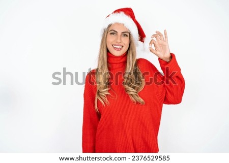 Beautiful hispanic woman wearing christmas hat and red knitted sweater hold hand arm okey symbol toothy approve advising novelty news