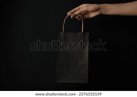 Paper shopping bag in hand on black background.