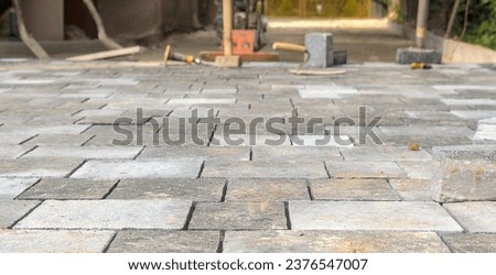 Laying concrete paving stones. The driveway. Paving utensils visible in the background.Laying paving stones on a long driveway. In the blurry background, visible paving tools: a compactor, etc. Royalty-Free Stock Photo #2376547007
