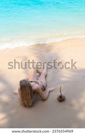 A woman in a swimsuit lies on the sand in the shade of a palm tree and looks at the sea. Vacation in tropical countries.