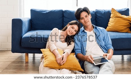 An attractive married man holding a tablet and a woman sit on the floor together in the living room looking at the camera at the new home. A family spends quality time together after home moving. Royalty-Free Stock Photo #2376578537