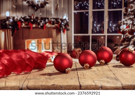 Wooden table of free space and christmas balls. Home interior with fireplace and christmas tree. Magic time. Empty space for your decoration. 