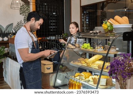Small business couple lifestyle concept, Asian coffee shop owner man or worker checking online bakery order by using tablet, barista woman making coffee by modern machine, Check stock for sale.