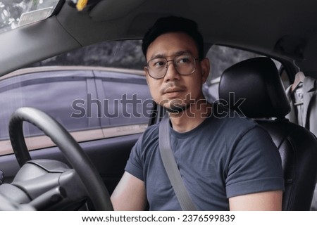 Asian Thai man with beard, wear eyeglasses and navy t-shirt, parking a car by turn his face looking at back side, driving training for safety. pick up girlfriend after work.
