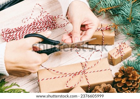 Woman wrapping christmas present , girl prepares xmas gifts with fir tree and pine cone. Hand crafted gift on wooden background with Christmas decor. Top view, copy space. Toned.