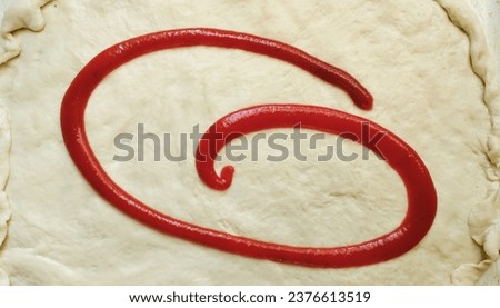 The letter G written with ketchup on rolled out dough. High quality stock photo.