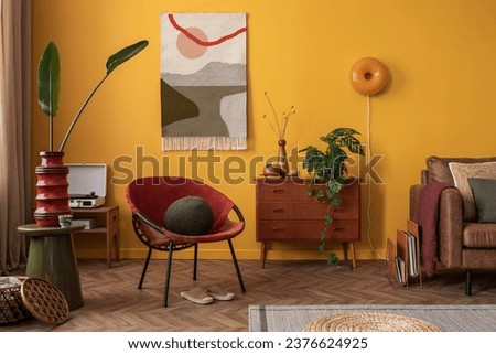 Aesthetic composition of warm and cozy living room interior with stylish kilim rug, wooden sideboard, plant, yellow wall, red armchair, brown sofa and personal accessories. Home decor. Template. Royalty-Free Stock Photo #2376624925