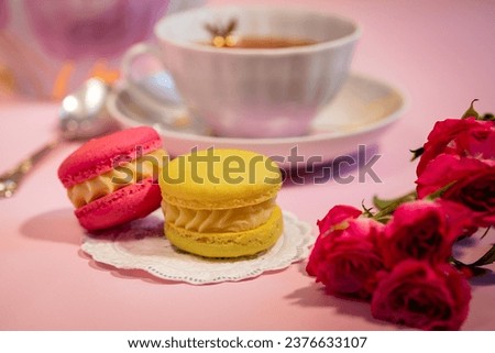 Delicious French macaroon dessert close-up. Colorful macaroons, flowers and tea, bright yellow-pink shades. Concept of cheerful sunny morning and breakfast