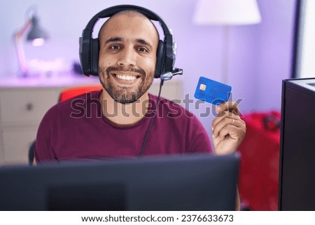 Hispanic man with beard doing online shopping with computer and credit card looking positive and happy standing and smiling with a confident smile showing teeth 