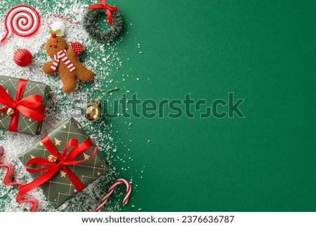 Christmas wonderland top view: Green presents, gleaming baubles, gingerbread man ornament, ringing bells, dainty wreath, candy cane, lollipop, snow against a green backdrop with text space Royalty-Free Stock Photo #2376636787
