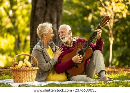 Senior people having fun in the park playing guitar and singing songs.
