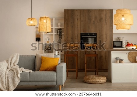 Interior of modern open plan kitchen with island table, grey sofa and glowing lamps Royalty-Free Stock Photo #2376646011