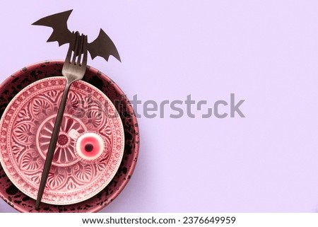 Halloween table setting with eye and paper bat on purple background, closeup