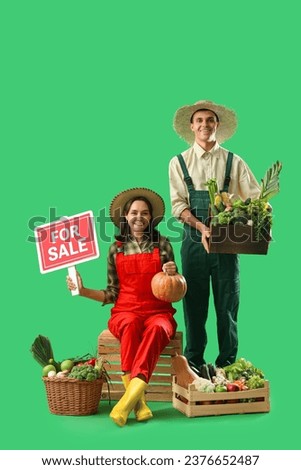 Young farmers with fresh vegetables and FOR SALE sign on green background