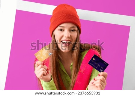 Young woman with credit cards and frame on purple background