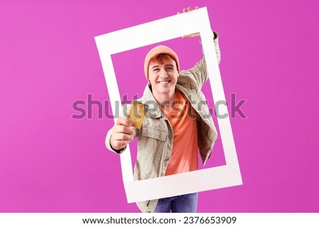 Young man with credit card and frame on purple background