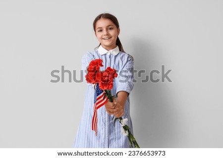Little girl with USA flag and flowers on light background. Veterans Day celebration