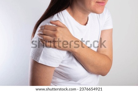 A girl in a white T-shirt is holding her shoulder joint and is in severe pain. Concept of habitual shoulder dislocation. Improper rehabilitation, surgery to treat a dislocated shoulder. Royalty-Free Stock Photo #2376654921