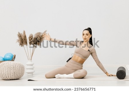 Attractive slim girl using a roller to relax her body muscles after a workout. A young fit woman in light sportswear posing against a light background.