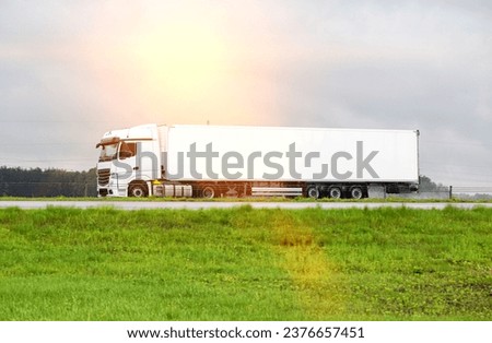 A beautiful new white semi-trailer truck transports cargo along the road in summer. Concept of commercial cargo transportation, logistics services. Trucking business. Side view Royalty-Free Stock Photo #2376657451