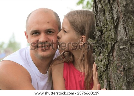 Cute white little girl kissing her handsome father's cheek. Cheerful teenage girl having fun with her father. Happy family spending exciting time outdoors 