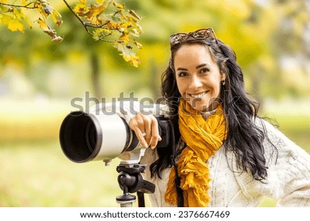 A professional female photographer stands next to her camera, taking pictures of autumn portraits or landscapes.