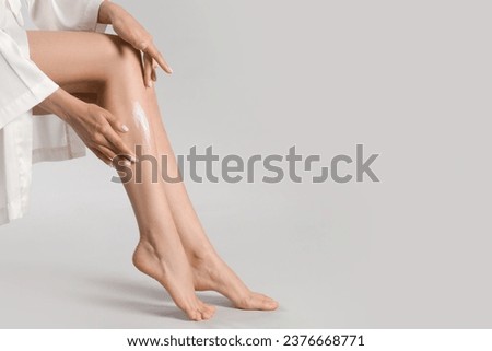 Woman applying body cream onto her smooth legs on light grey background, closeup. Space for text Royalty-Free Stock Photo #2376668771