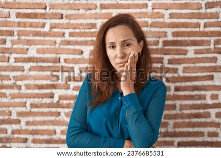 Brunette woman standing over bricks wall thinking looking tired and bored with depression problems with crossed arms. 