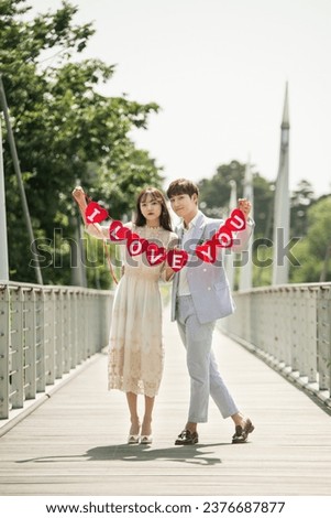 A young male and female couple are enjoying themselves while taking wedding pictures on the bridge with a placard.
