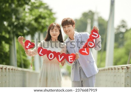 A young male and female couple are enjoying themselves while taking wedding pictures on the bridge with a placard.