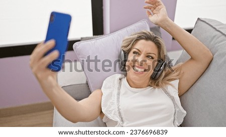 Young blonde woman listening to music make selfie by smartphone at home