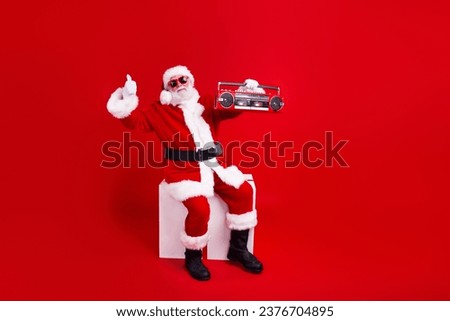 Photo of satisfied cheerful man santa claus wear sunglass hold retro radio thumb up recommendation isolated on red color background